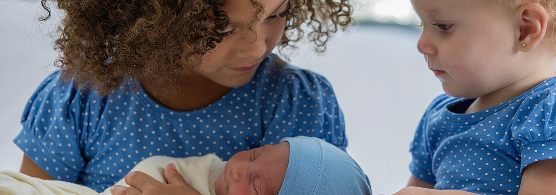 Mixed race siblings look at newborn baby boy or girl